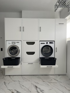Weißer Waschmaschinenschrank mit ausgezogener Platte für Waschkörbe und passendem Schrank für diese.